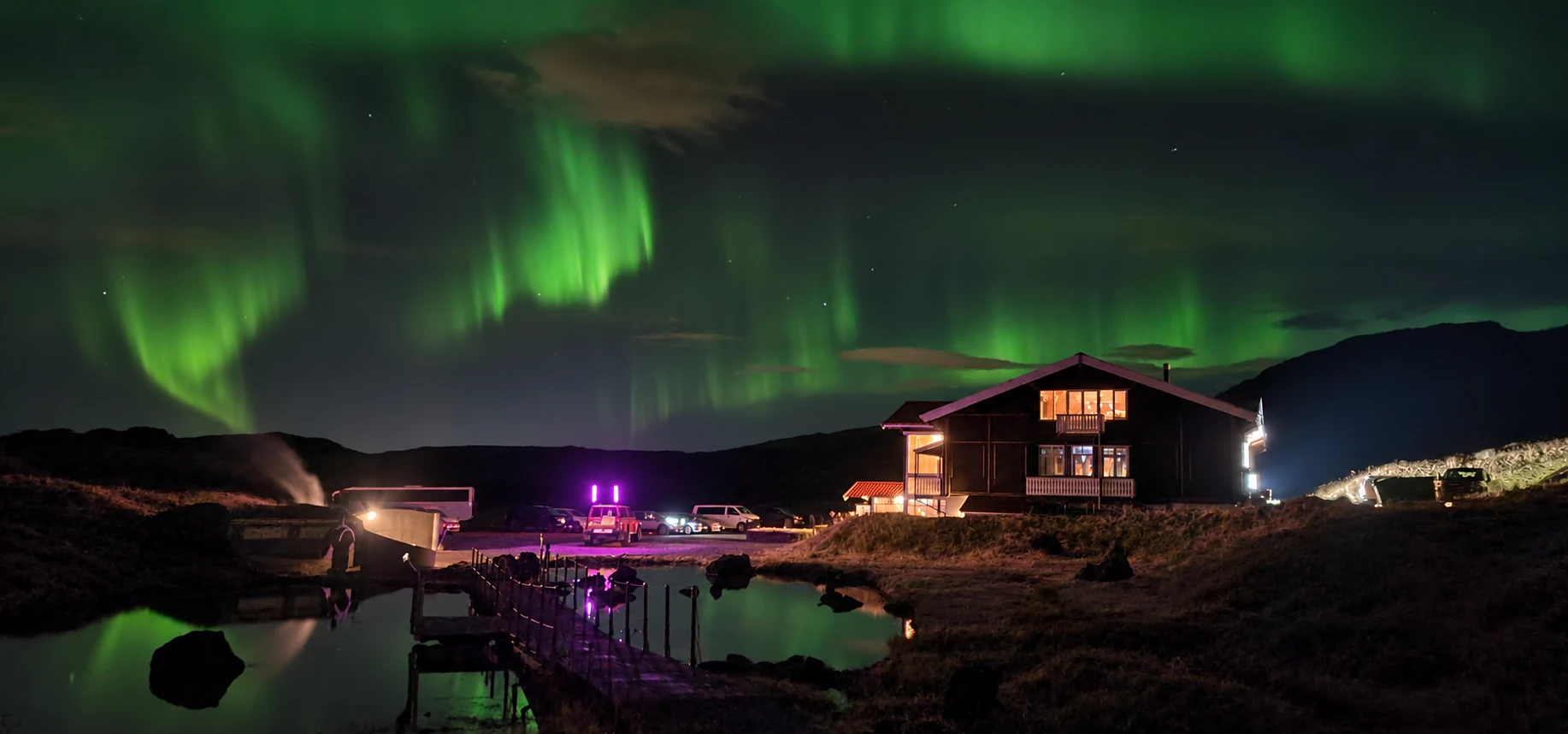 Green northern lights above the Hveradalir lodge, geothermal pools and walkway at night